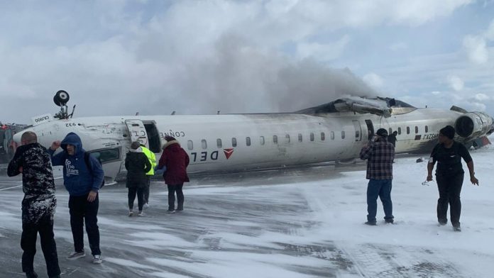 Mitsubishi CRJ-900LR upside down on the snowy tarmac as emergency workers hose it down.